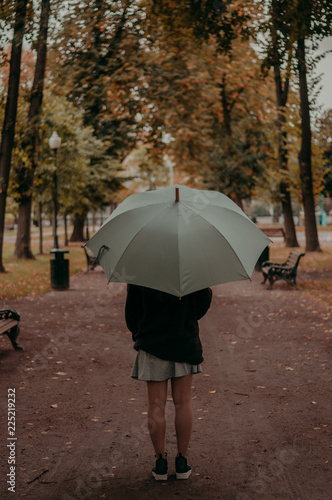Young woman with blue umbrella in the alley in the autumn park