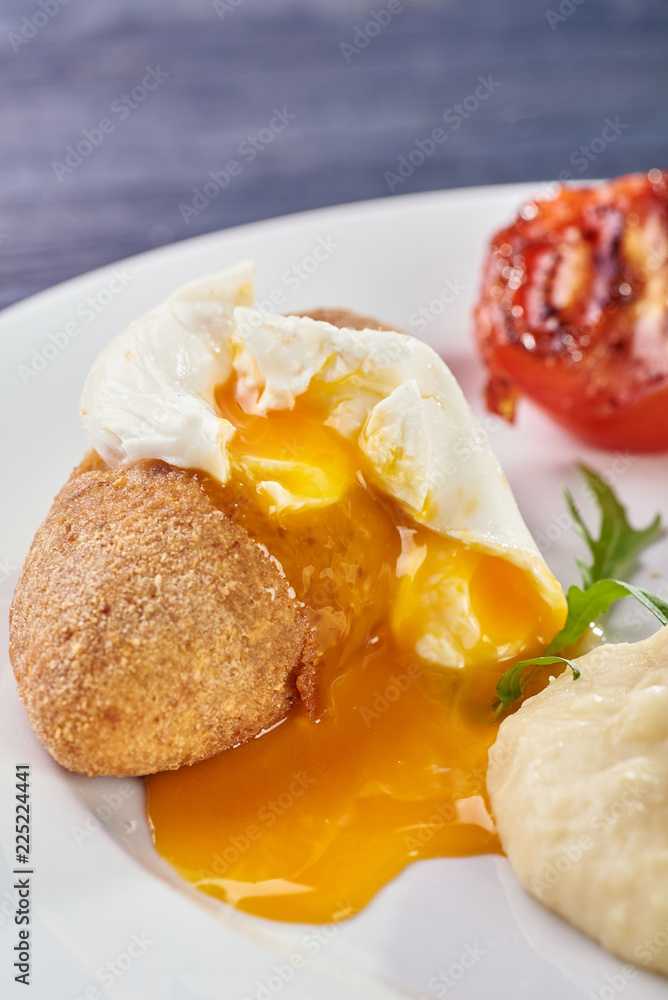 A full-fledged hot dinner on a white plate in a cafe, restaurant. Chicken Kiev stuffed with breaded, poached eggs, grilled tomato, arugula and mashed potatoes for dinner.