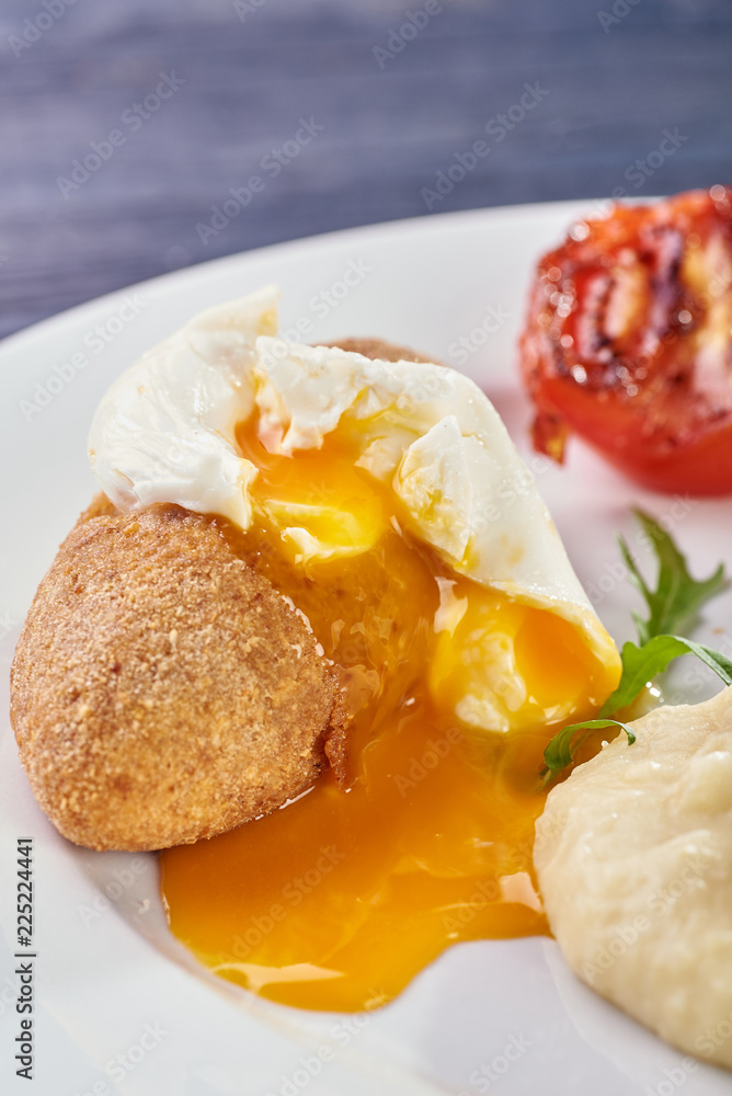 A full-fledged hot dinner on a white plate in a cafe, restaurant. Chicken Kiev stuffed with breaded, poached eggs, grilled tomato, arugula and mashed potatoes for dinner. A full-fledged hot dinner on a white plate in a cafe, restaurant. Chicken Kiev stuffed with breaded, poached eggs, grilled tomato, arugula and mashed potatoes for dinner.