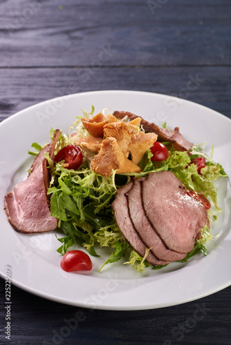 A hearty nice salad for the festive table. Slices of salted meat, bacon, beef, veal, pork from oven, meat sausage, ham. Appetizer from greenery, arugula, mushrooms chanterelles and cherry tomatoes.