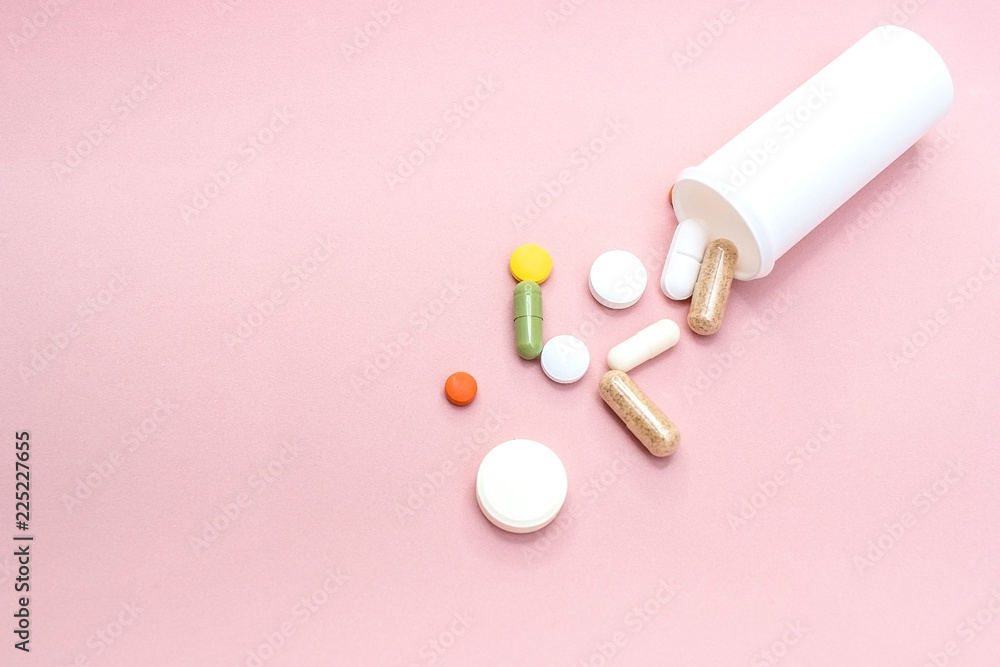 Tablets and pills from a bottle on a pink background Tablets and pills from a bottle on a pink background