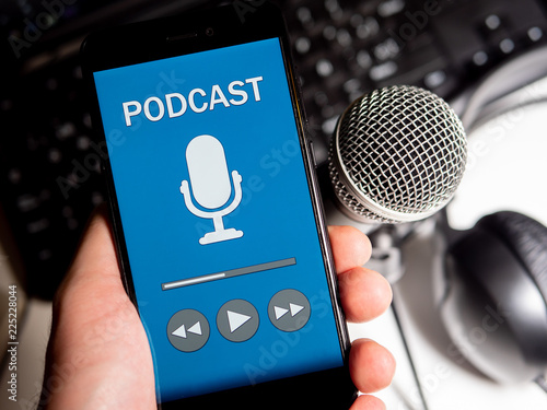 Listening podcast in phone with microphone, headphones and keyboard on white desktop. First person point of view