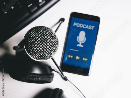 Phone with podcast livestream with microphone, headphones and keyboard on white table. Top view