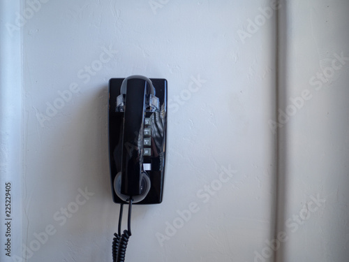 Black landline phone and receiver hanging on white wall