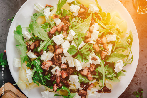 Top view of a plate with food. A dish of pasta, rucola and spices, next to the ingredients of food, garlic, tomatoes on a stone, dark countertop. The concept of preparing food.