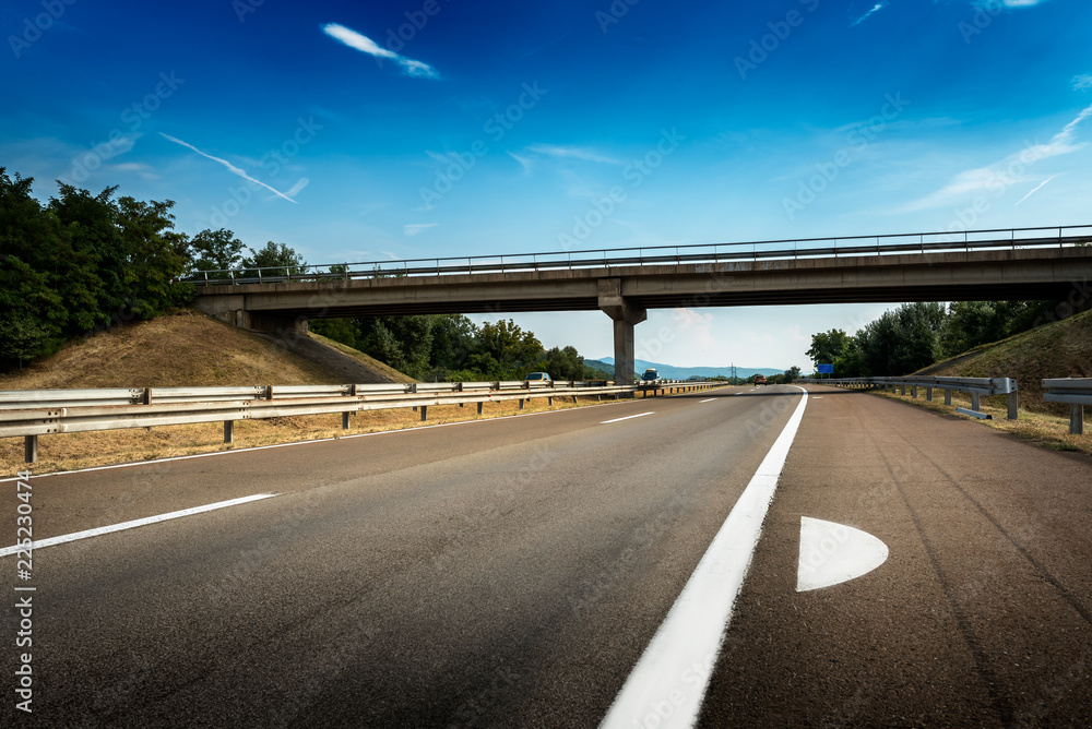 Fototapeta premium View of a multi lane highway with fog markings and a crossing in distance