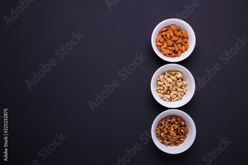 Three bowls with different nuts on a black table