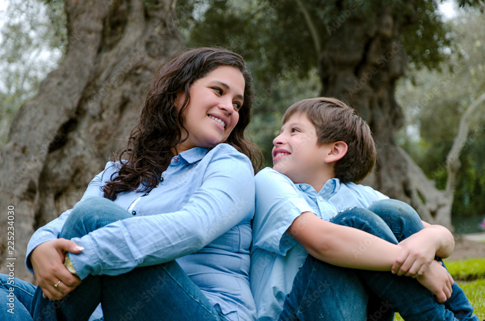 Mom and son sitting on green grass in green park. Concept of happy family relations Mom and son sitting on green grass in green park. Concept of happy family relations