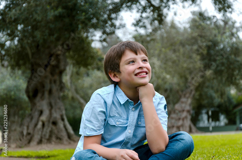 Cute little boy sitting in the park smiling thinking