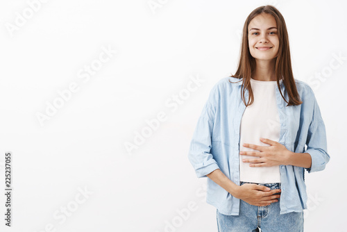 Sound mind in healthy body. Portrait of delighted joyful young european female taking care of health touching belly or stomach with pleased happy smile taking vitamins or drinking yoghurt photo