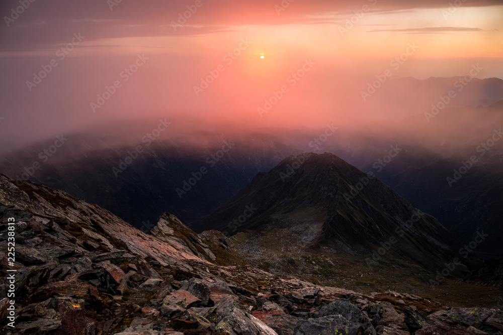 Sunrise lights paint clouds over a foggy landscape in an adventure journey in the Italian Alps