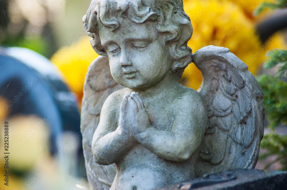 closeup of stoned angel on tomb in a cemetery on yellow flowers background closeup of stoned angel on tomb in a cemetery on yellow flowers background