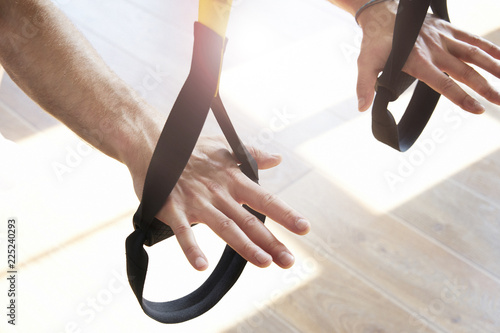 Close-up of man hands doing exercise alone with fitness belts in modern gym club, workout single sport, sun shining.
