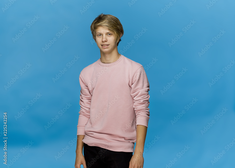 Handsome happy smiling young man wearing pink blouse studio portrait against blue wall Handsome happy smiling young man wearing pink blouse studio portrait against blue wall