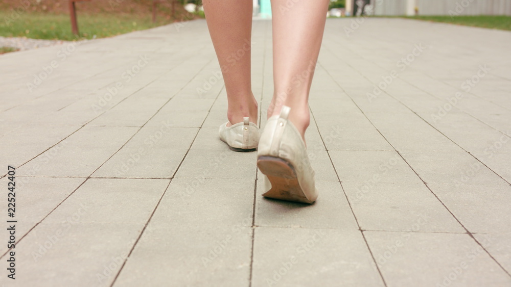 A young girl is shot in slippers strolling on a summer day, close-up on her feet from the back. Dolly shot