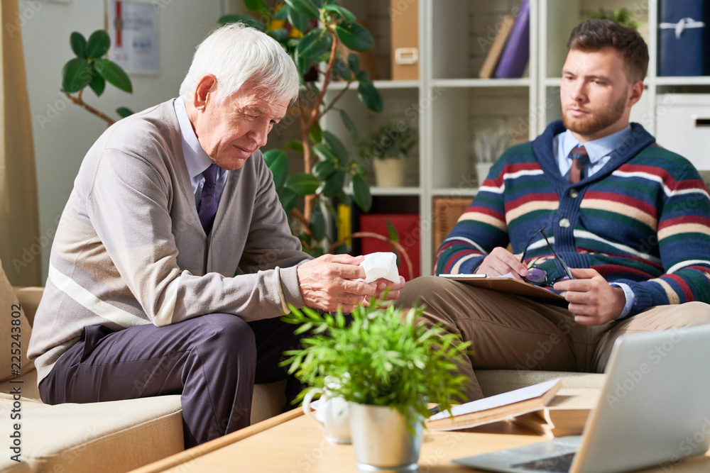 Side view portrait of senior man holding tissues sharing mental problems with psychologist during therapy session, copy space Side view portrait of senior man holding tissues sharing mental problems with psychologist during therapy session, copy space