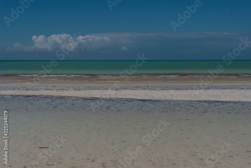 Stripes of white shallow water, white sand, and aqua seas under a deep blue sky with a dramatic line of clouds over the horizon paint a picture of a tropical paradise on Isla Holbox, Mexico.