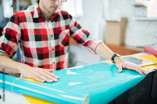 Close-up of busy concentrated young man in checkered shirt touching glossy paper while checking quality in typography