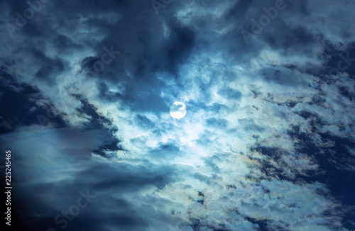 The full moon in the night sky hiding behind the clouds. © Yuri Bizgaimer