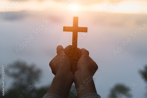 Silhouette off hands holding wooden cross  on sunrise background, Crucifix, Symbol of Faith.