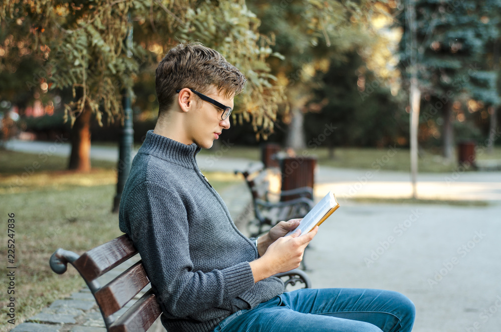 Teenager sitting on park bench and reading a book Teenager sitting on park bench and reading a book