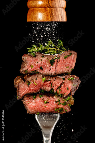 Sliced beef steak from grill on a fork. Salt is strewing from wooden mill
