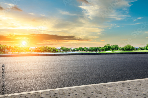 Empty asphalt road and green forest with colorful clouds at sunset