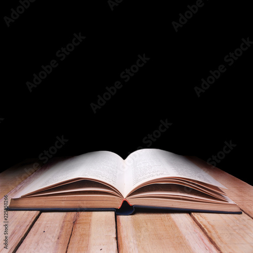 Opened Book on Wooden Table Against Black Background