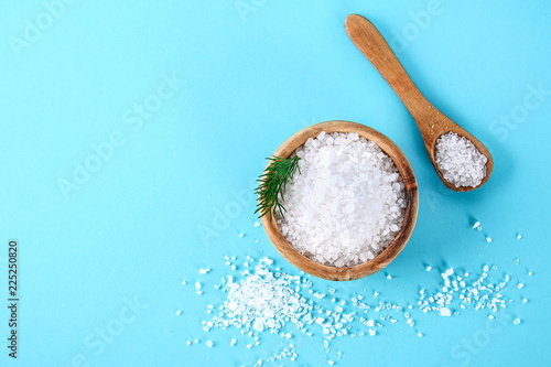 Crystals of large sea salt in a wooden bowl and spoon and dill on a blue table. photo