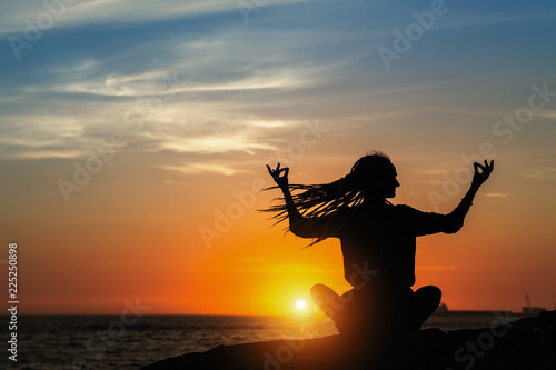 Yoga silhouette meditation girl on the ocean during amazing sunset.