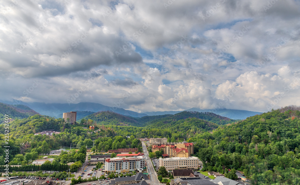 The green Smoky Mountains and Gatlinburg, TN as seen from an observation deck in summer with white and grey clouds and blue sky