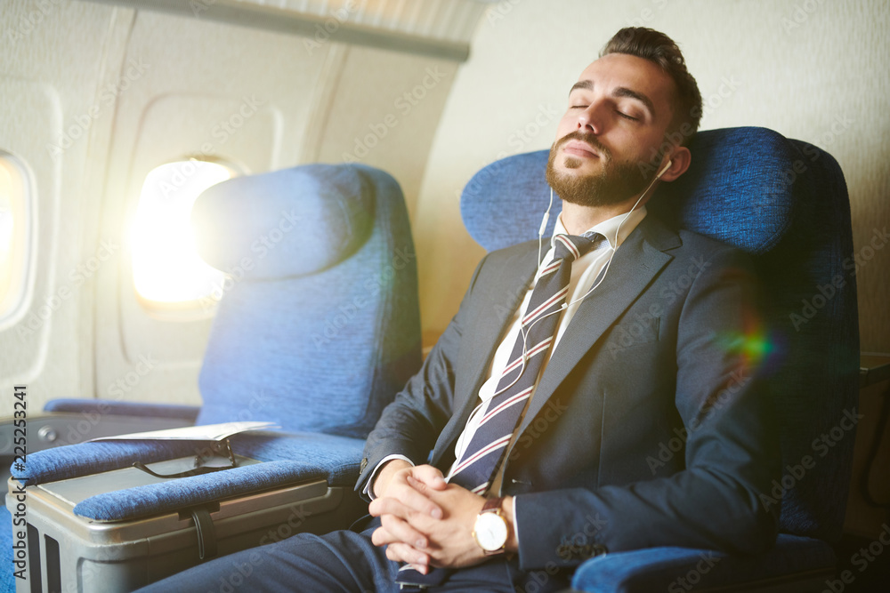 Naklejka premium Portrait of handsome bearded businessman wearing earphones sleeping blissfully while enjoying first class flight in plane, copy space
