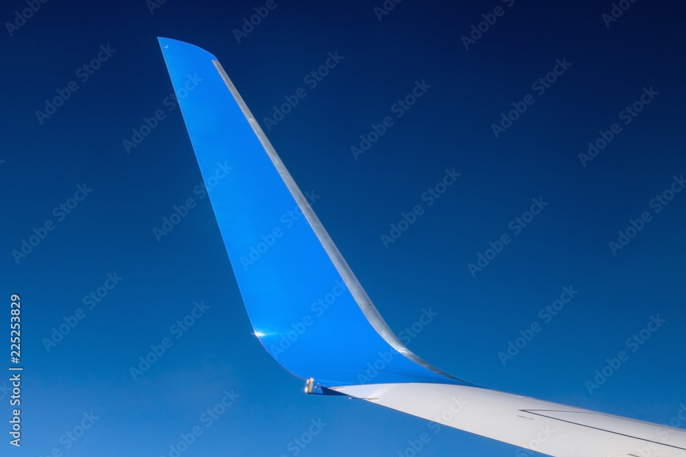 Fototapeta premium The blue winglet on a wing of plane when a flight in a blue sky. Part of jet wing, close view.