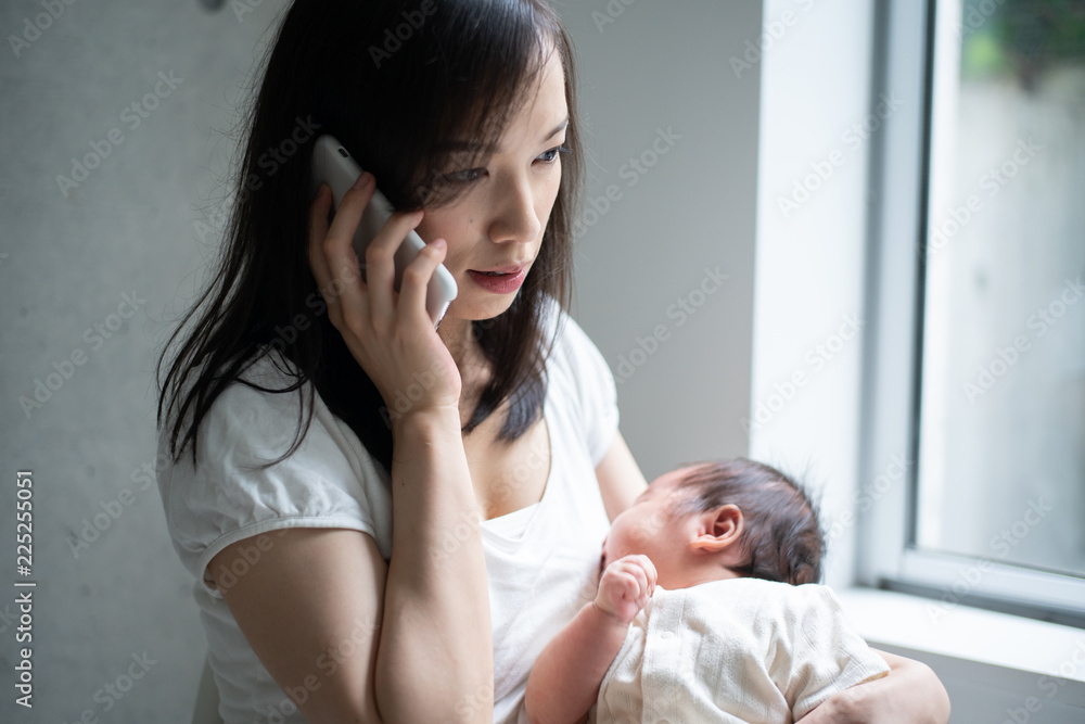 赤ちゃんを抱きながら電話をかける女性 赤ちゃんを抱きながら電話をかける女性