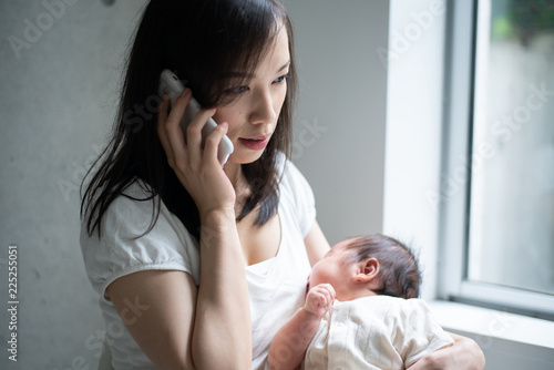赤ちゃんを抱きながら電話をかける女性 © blanche