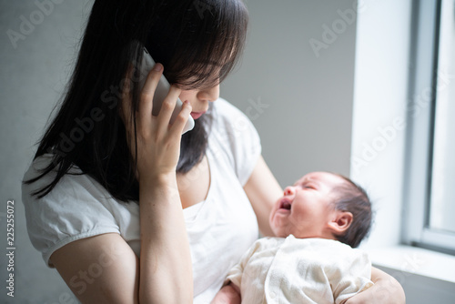 赤ちゃんを抱きながら電話をかける女性