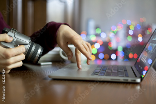 young male photographer holding a camera and prcessing his photos on laptop in the studio f photo