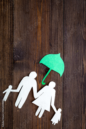 Illustration of social security concept. Financial protection. Family silhouette, cutout under umbrella on dark wooden background top view space for text photo