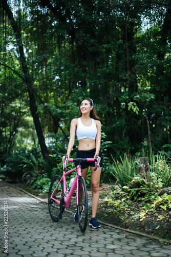 Portrait of young beautiful woman with pink bike in the park. Actractive healthy woman. photo