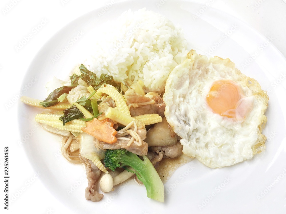 Stir fry chicken, sweet peppers, corn, broccoli, sweet basil and green beans with rice and fried egg in ธhai style in white dish on white background. Thai style food. Stir fry chicken, sweet peppers, corn, broccoli, sweet basil and green beans with rice and fried egg in ธhai style in white dish on white background. Thai style food.
