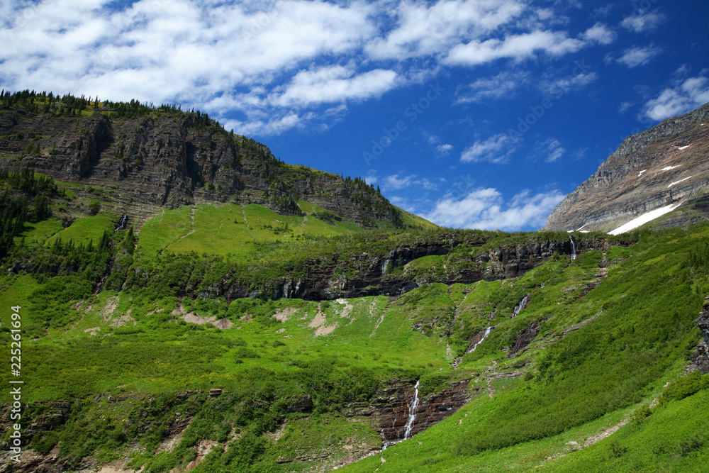 Naklejka premium Green grass and waterfalls along the Going to the Sun Road in Glacier National Park, Montana, USA