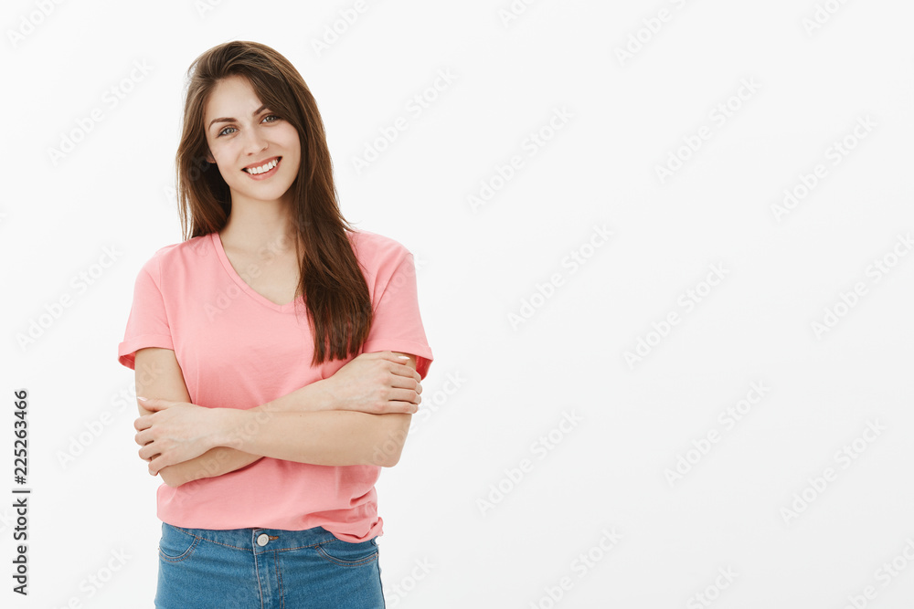 Girl trying to control emotions. Portrait of charming timid female european in pink t-shirt, hugging herself and smiling broadly, feeling shy and unsure while talking with stranger in office Girl trying to control emotions. Portrait of charming timid female european in pink t-shirt, hugging herself and smiling broadly, feeling shy and unsure while talking with stranger in office