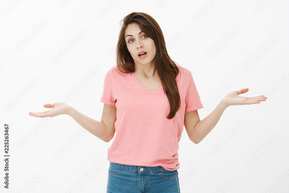 Portrait of unaware clueless beautiful brunette in pink stylish t-shirt, shrugging and spreading palms aside in confused and questioned gesture, answering question, having no idea what to do Portrait of unaware clueless beautiful brunette in pink stylish t-shirt, shrugging and spreading palms aside in confused and questioned gesture, answering question, having no idea what to do