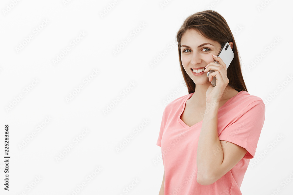 Talkative girl always takes phone for walk. Portrait of good-looking joyful female in casual outfit holding smartphone near ear and gazing with broad smile at camera while talking with friend Talkative girl always takes phone for walk. Portrait of good-looking joyful female in casual outfit holding smartphone near ear and gazing with broad smile at camera while talking with friend
