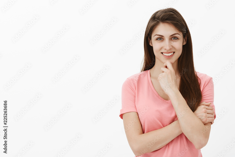 Young female entrepreneur with brunette hair in pink t-shirt smiling joyfully and touching chin while thinking, making up interesting idea and being intrigued with fulfillment of future plan Young female entrepreneur with brunette hair in pink t-shirt smiling joyfully and touching chin while thinking, making up interesting idea and being intrigued with fulfillment of future plan