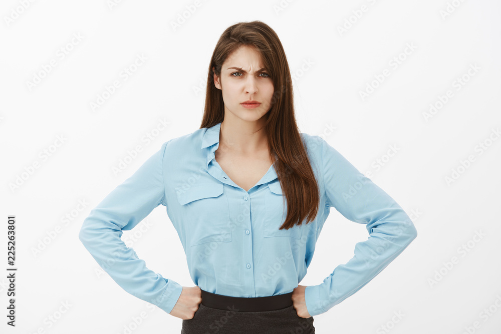Disgrace for our company. Portrait of angry displeased bossy woman in blue blouse, holding hands on hips and frowning, sulking from disappointment, being offended or upset, standing over grey wall