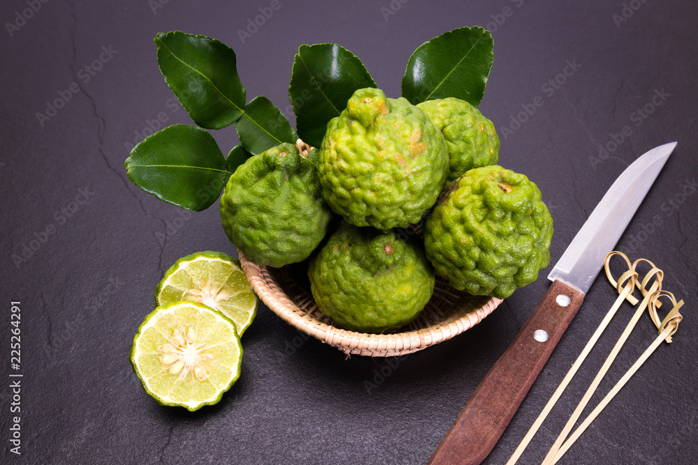 Bergamot, kaffir lime and kaffir lime leaf with basket and knife on dark background Bergamot, kaffir lime and kaffir lime leaf with basket and knife on dark background