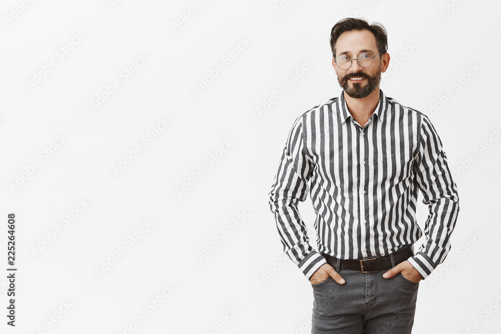 Fototapeta premium Successful and confident male entrepreneur in stylish outfit and glasses holding hands in pockets and smiling joyfully, giving speech in front students, teaching how to gain money and fame
