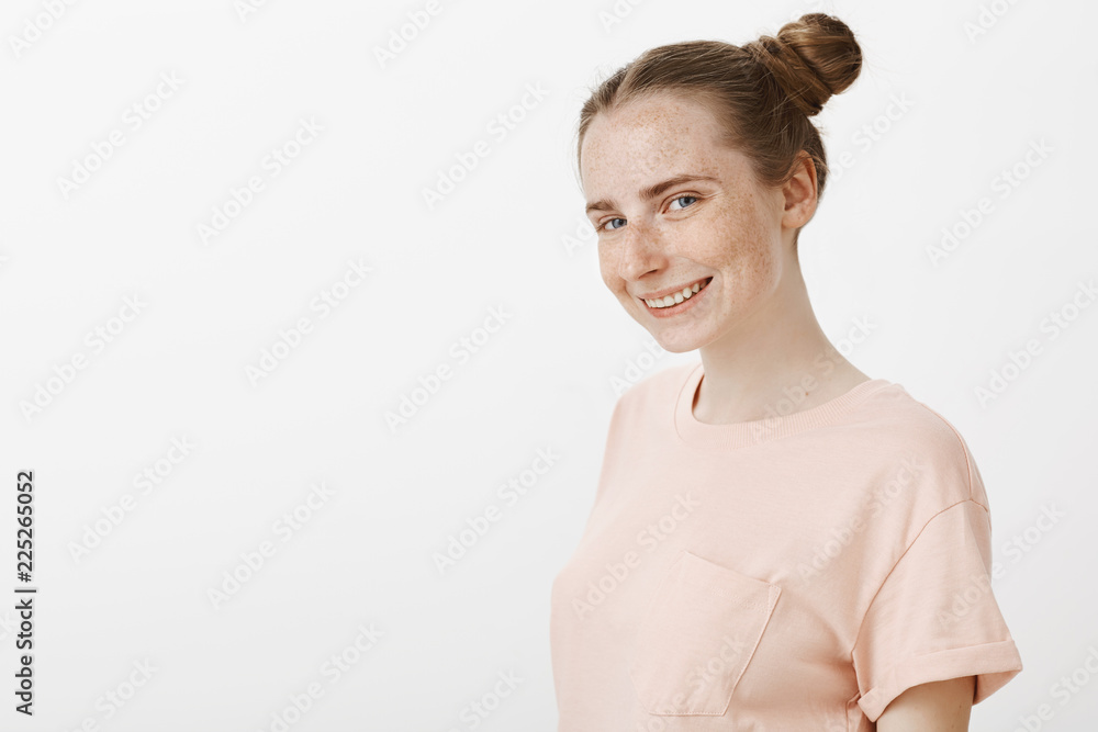 Waist-up shot of curious charming young woman with funny buns hairstyle standing half-turned over gray background and gazing with some interesting intention at camera, having idea in mind, smiling Waist-up shot of curious charming young woman with funny buns hairstyle standing half-turned over gray background and gazing with some interesting intention at camera, having idea in mind, smiling