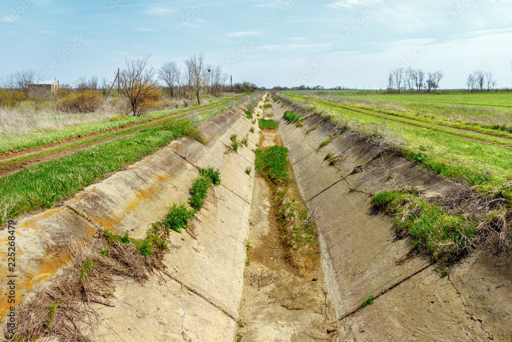 The dry concrete irrigation channel in the green farmland